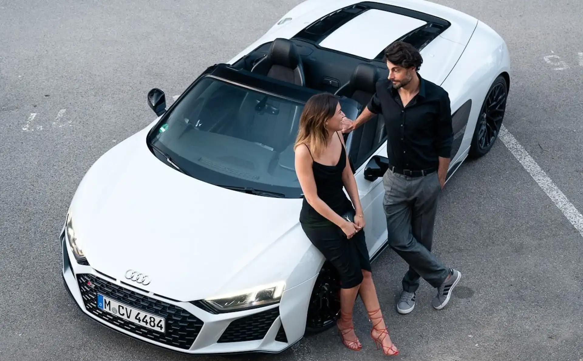 A couple leans on a white Audi R8 Convertible.